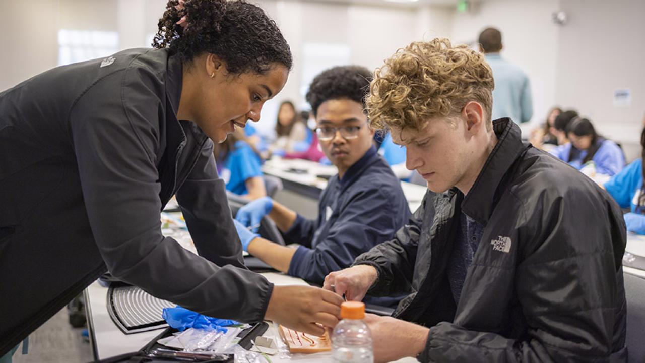 Elise Fannon, general surgery research resident at UC Davis Health, shows AvenueM students some tricks for suturing. 